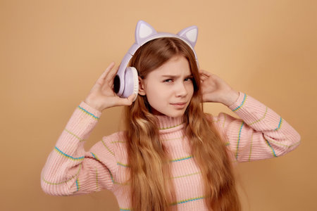 Tricky little girl in headphones with ears eavesdrop on beige backgroundの写真素材