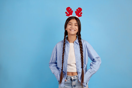 Smiling teenage girl with decorative deer horns and pigtails on blue background.の写真素材