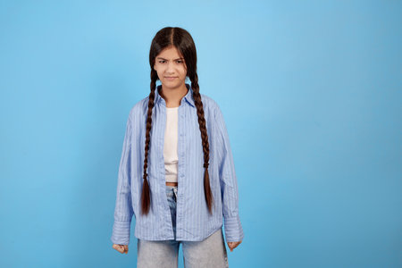 Teenage girl looks malcontent and dissatisfied on blue background.の写真素材