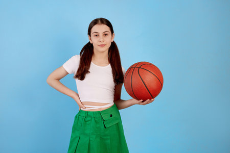 Young brunette teenage girl with basket ball and ponytails on blue background.の写真素材