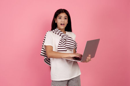 Young shocked teenage girl and laptop on pink background in studio.の写真素材