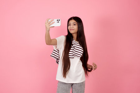 Young smiling teenage girl taking a selfie with phone on pink background in studio.の写真素材