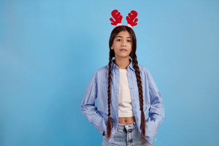 Confident teenage girl with decorative deer horns and pigtails on blue background.の写真素材