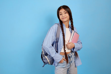 Young smiling teenage girl holding books and notebooks with bag on blue background.の写真素材