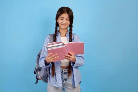 Teenage girl books and notebooks with bag and smiling on blue background.の写真素材