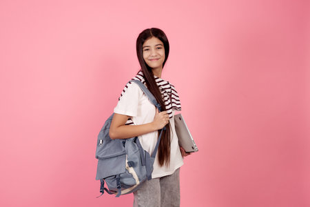 Young smiling teenage girl with bag and laptop on pink background in studio.の写真素材
