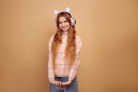 Smiling and shy little girl in headphones with ears on beige backgroundの写真素材