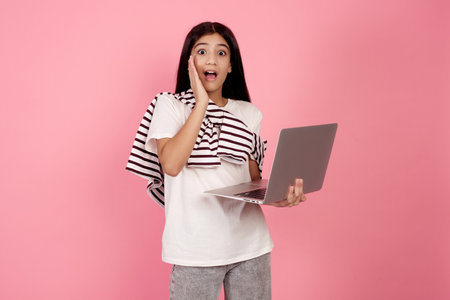 Young shocked teenage girl and laptop on pink background in studio.の写真素材