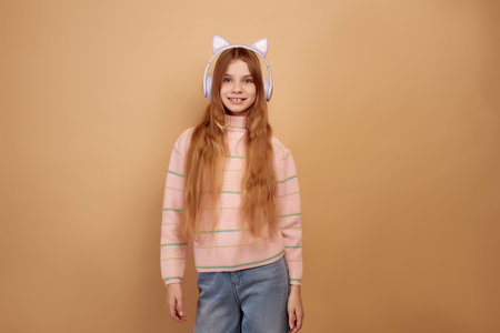Smiling little girl in headphones with ears on beige backgroundの写真素材