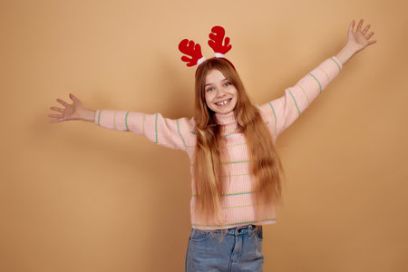 Smiling girl in decorative deer horns dancing on beige background.の写真素材