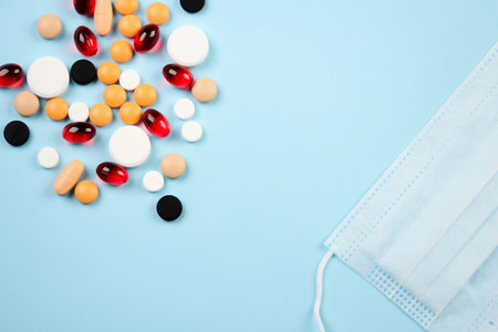 Disposable medical mask and blister with white pills lie on a blue background
