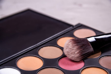 Makeup brushes, open can with blush palette of eyeshadows on a gray background, top view