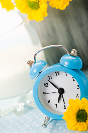 Blue alarm clock with glass of milk and yellow flowersの写真素材