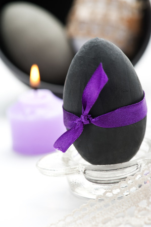 Black Easter egg with purple bow and candleの写真素材