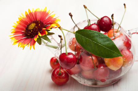 Translucent pot of red and yellow cherries on white woden backgroundの写真素材