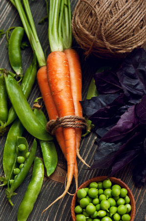 Still life with raw carrots, green peas and basil on dark wooden table の写真素材