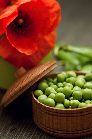 Close-up of green peas in bowl on dark wooden background with red poppy flowerの写真素材