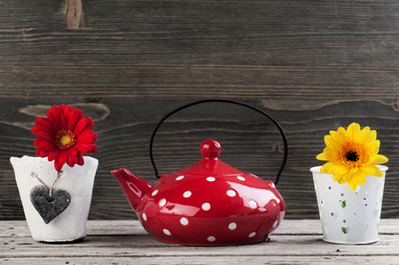 Red polka dot teapot, red and yellow flower in pot on wooden background. Place for text. Toned imageの写真素材
