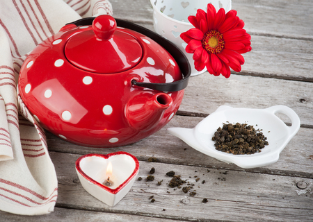 Polka dot red tea pot, leaves, candle and flower on the weathered wooden table. Tea time conceptの写真素材
