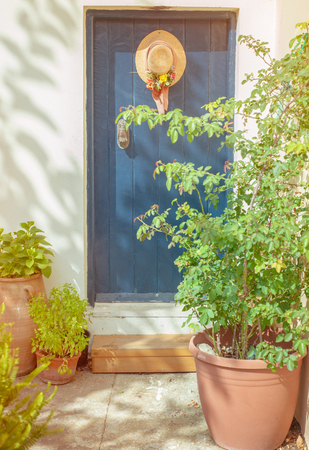 Old blue door with hat and garden flowers in beautiful sunny light with retro vintage. Toned imageの写真素材