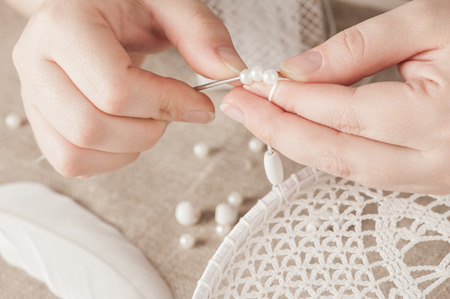 Close-up of female hands white dream catcher. Handmade workshop composition of beads, threads, tools for DIYの写真素材