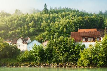 Alps and fog in early morning sun. Landscape with mountains, river, pines and alpine houseの写真素材