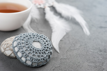 Cup of tea and crocheted pebbles closeup on concrete background. Shallow focus, toned imageの写真素材