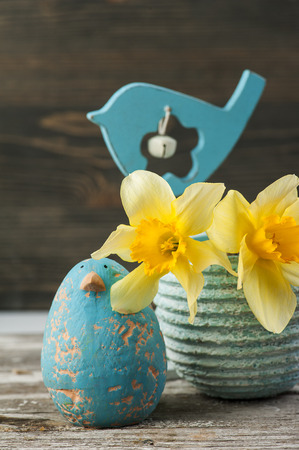 Daffodil flowers in pot with gardening tools on wooden table with blue clay birdの写真素材