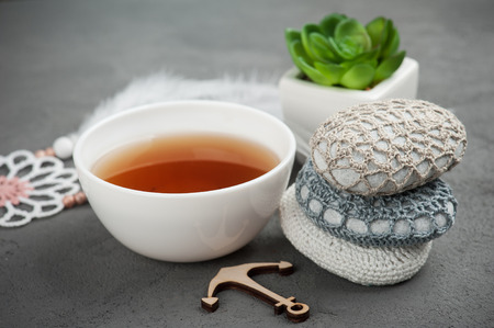 Cup of tea and crocheted pebbles closeup on concrete background. Shallow focus, toned imageの写真素材