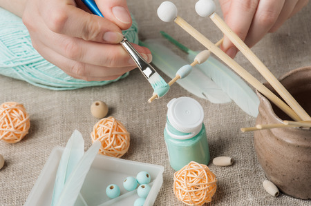 Close-up of female hands painting wooden beads, having dream catcher assembled. Handmade workshop composition of feathers, beads, tools for DIYの写真素材