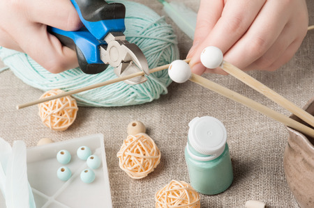 Closeup of female hands cutting wooden stick and mint threads on background. Handmade workshop composition of beads, threads, tools for DIYの写真素材