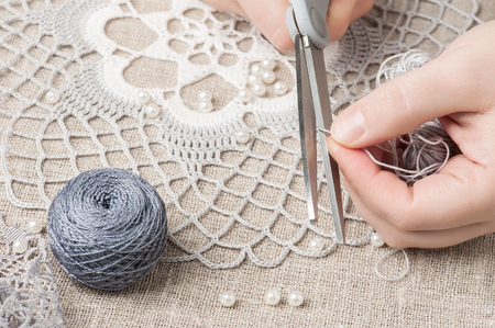 Closeup of female hands cutting thread and grey dream catcher background. Handmade workshop composition of beads, threads, tools for DIYの写真素材
