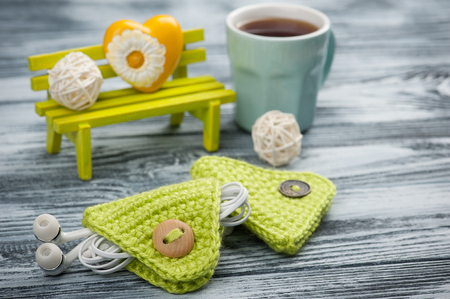 Cute green knitted ear pods cord holder on wooden table. Life style set with cup of coffeeの写真素材