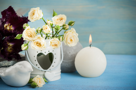 Vintage still life. Bouquet of white roses, purple tulips, blue wooden background and a burning candle, vintage decorの写真素材