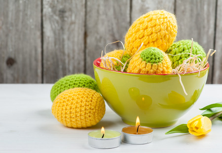 Green yellow crocheted easter eggs with lit candles and tulip on a white table backgroundの写真素材