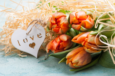Orange and green tulip couple with wooden heart on turquoise concrete rustic background. Lifestyle compisition for holidayの写真素材