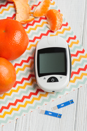 Close up of glucose meter and orange clemetines on white wooden background. Concept of health controlの写真素材