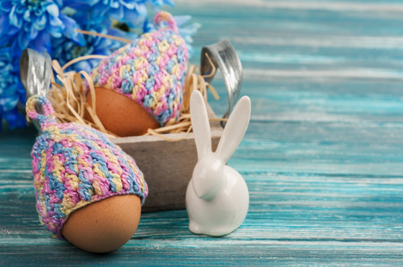 Easter composition with eggs in knitted hats, blue flowers and decorative rabbit on a wooden table. の写真素材