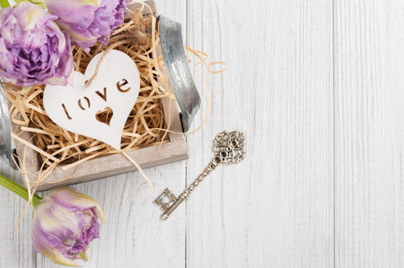 Wooden heart in vintage gift box with key and purple tulips on shabby white background. Copy space for textの写真素材