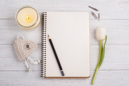 Open notebook, pencil, candle, earpods and tulip on white shabby wooden table. Concept for modern bloggingの写真素材
