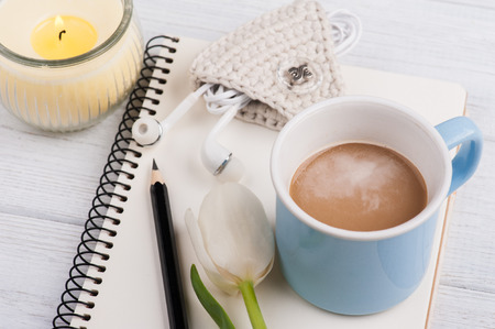 Open notebook, candle, earpods and mug of coffe on white shabby wooden table. Concept for modern bloggingの写真素材
