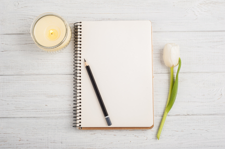 Open notebook, pencil, candle and tulip on white shabby wooden table. Concept for modern bloggingの写真素材