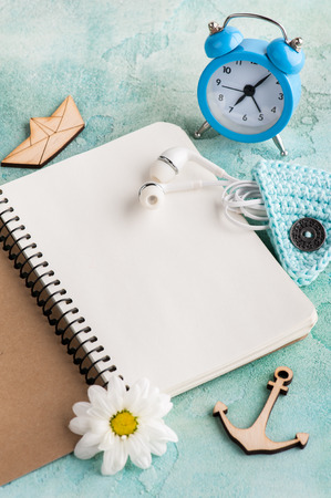 Open notebook, earphones, alarm clock, wooden boat and flower on blue shabby concrete table. Concept for modern bloggingの写真素材