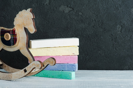 Vintage rocking horse next to black board and colorful chalk on wooden floorの写真素材
