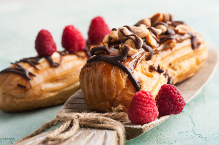 Eclairs with peanuts, chocolate icing and raspberries. Blue concrete background