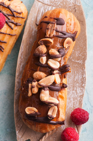 Eclairs with peanuts, chocolate icing and raspberries. Blue concrete background