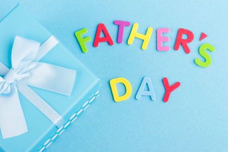 Blue gift box with ribbon on white wooden background. Father's day sign from colorful letters の写真素材