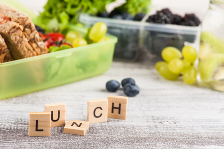 Vegetarian sandwich and berries in lunch box and fruits and vegetables on wooden table. Word Lunch on foregroundの写真素材
