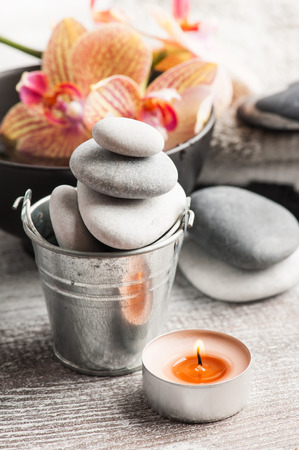 Spa still life with pebbles and red orange orchid, lit candle on wooden backgroundの写真素材