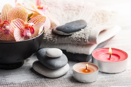 Spa still life with pebbles and red orange orchid, lit candle on wooden backgroundの写真素材